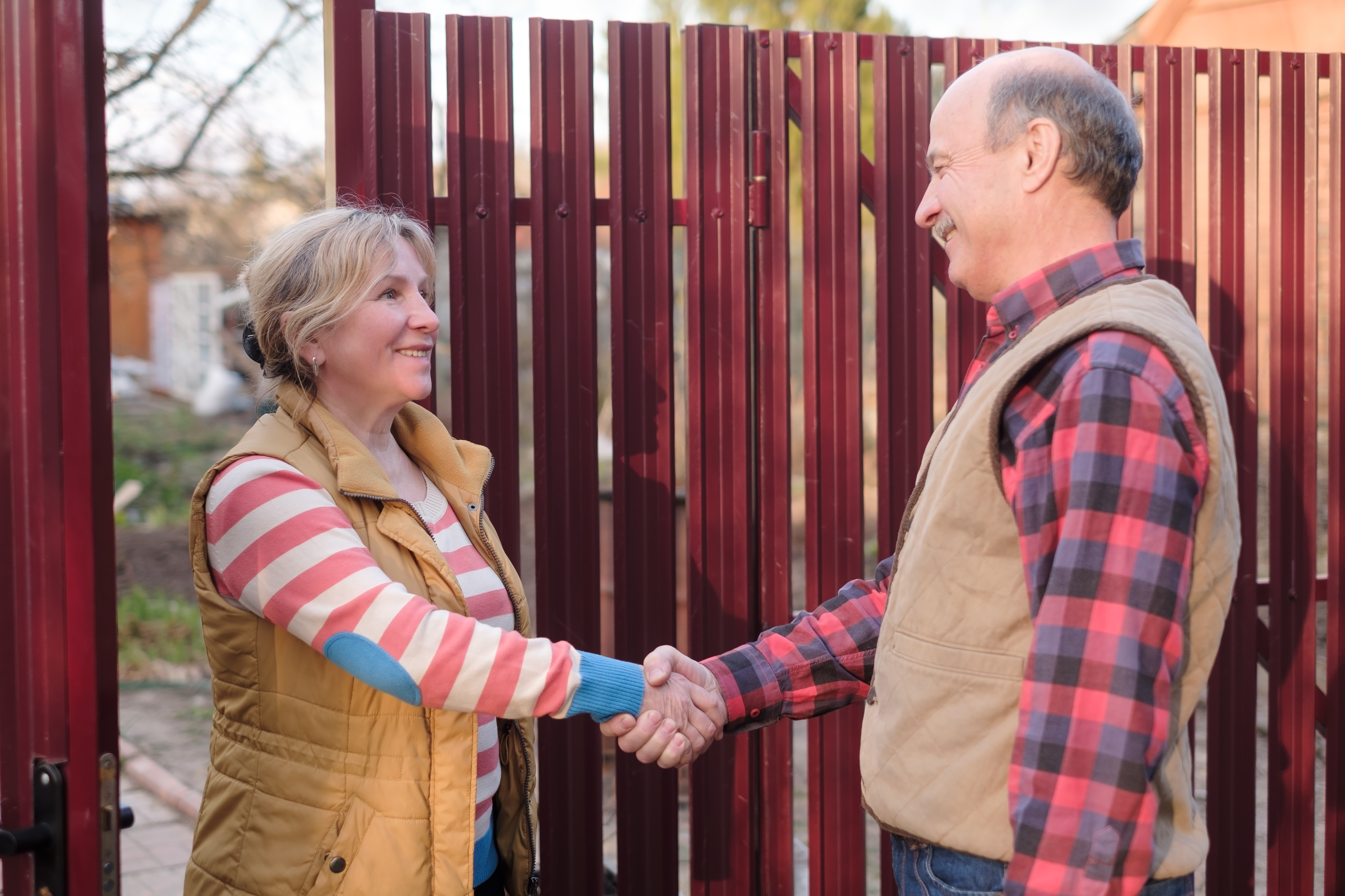 two senior neighbors man and woman talking to each other on sunny day near fence. They discuss important news